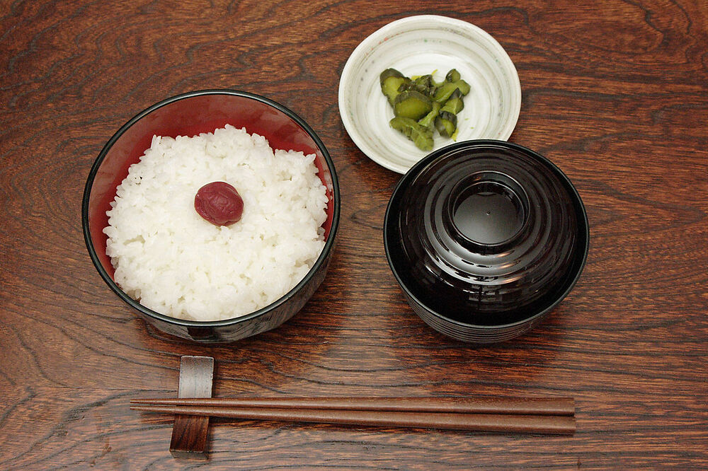 Japanese traditional meshi, 飯. A red umeboshi (dried ume, 梅干,) is on top of white rice. This is also called “Hinomaru rice.” It symbolizes the “circle of the sun” of the flag of Japan.